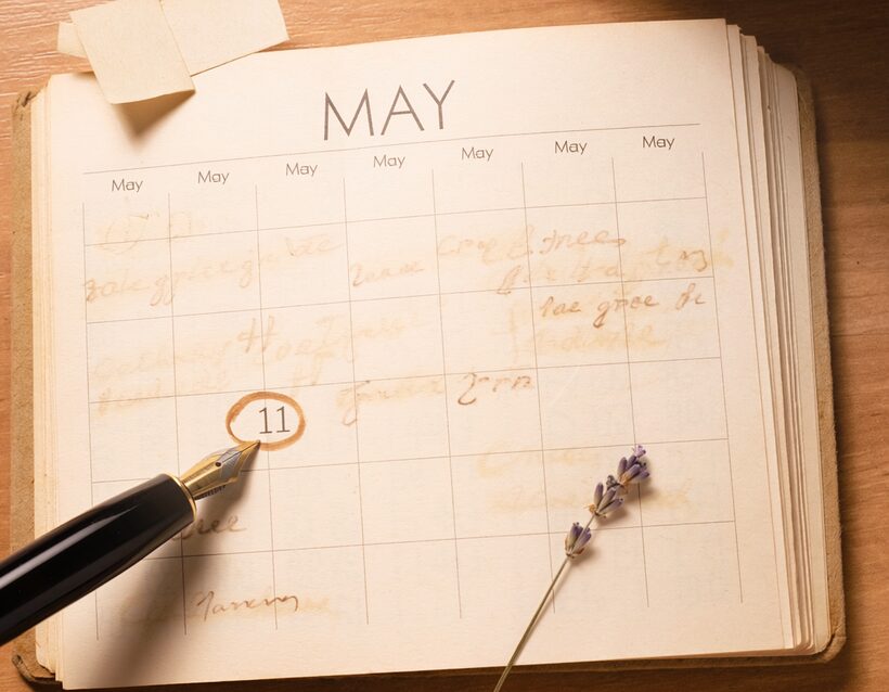 An overhead paper desk calendar opened to May, a fountain pen circling a date